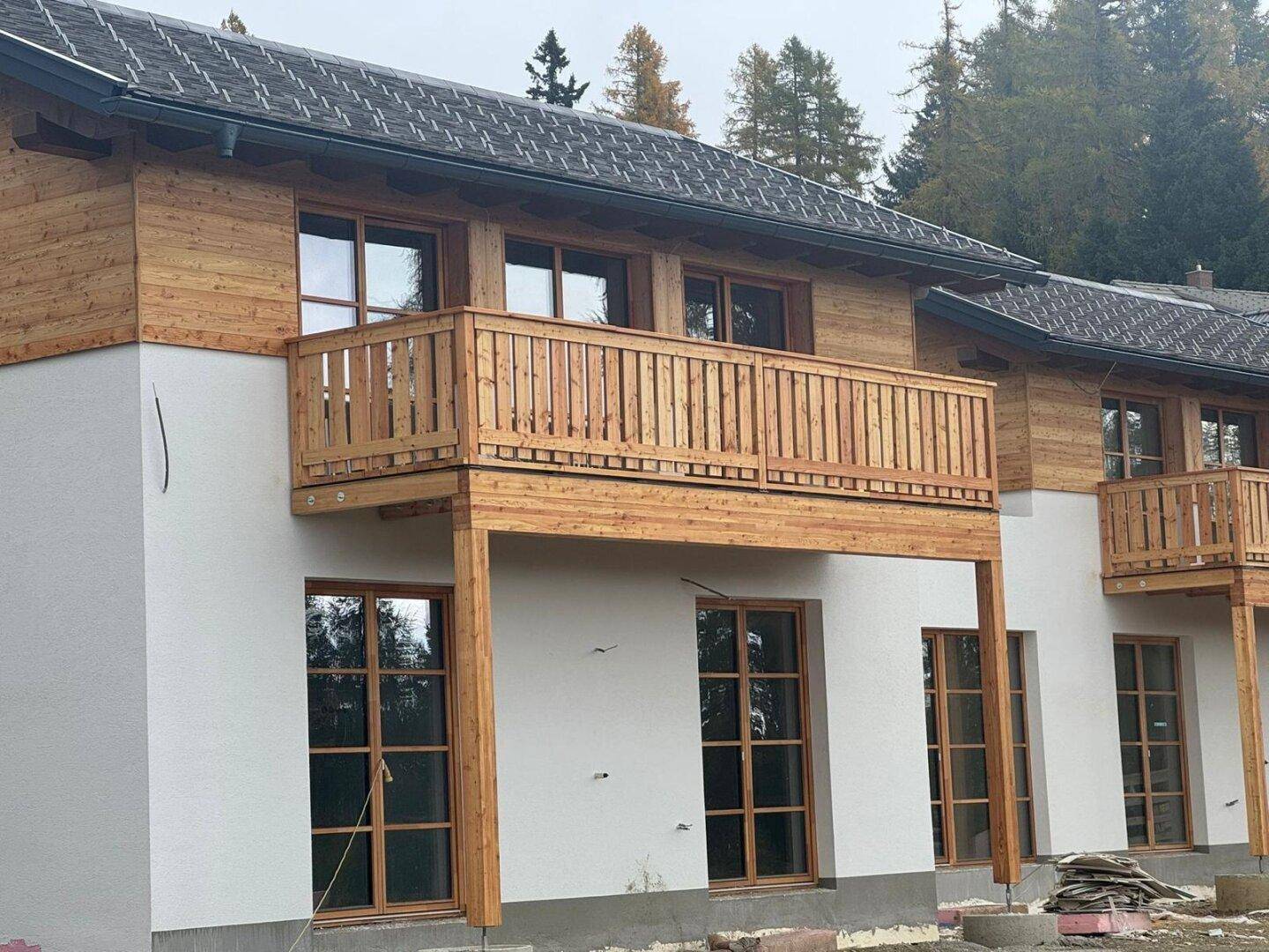 Reihe von modernen Chalets mit Holzverkleidung und Balkonen, umgeben von Bäumen und Natur.
