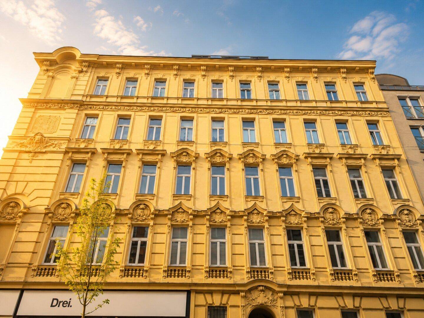 Historische gelbe Fassade eines Gebäudes mit vielen Fenstern und dekorativen architektonischen Details.