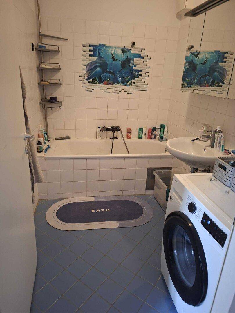 Badezimmer mit Badewanne, Waschbecken, Waschmaschine und blauen Bodenfliesen.