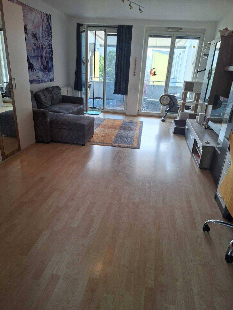 Helles Wohnzimmer mit hellem Laminatboden, gemütlichem Sofa und Zugang zu einem Balkon.