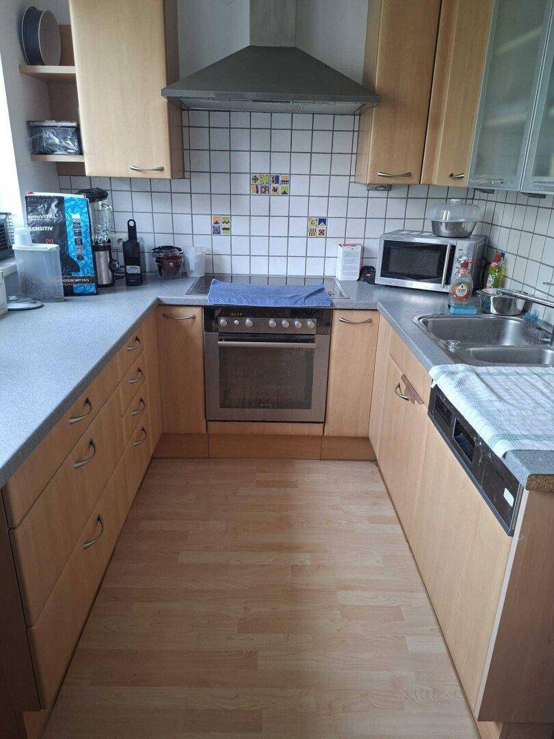 Funktionale Küche mit hellen Holzschränken, weißen Fliesen und integrierten Küchengeräten.