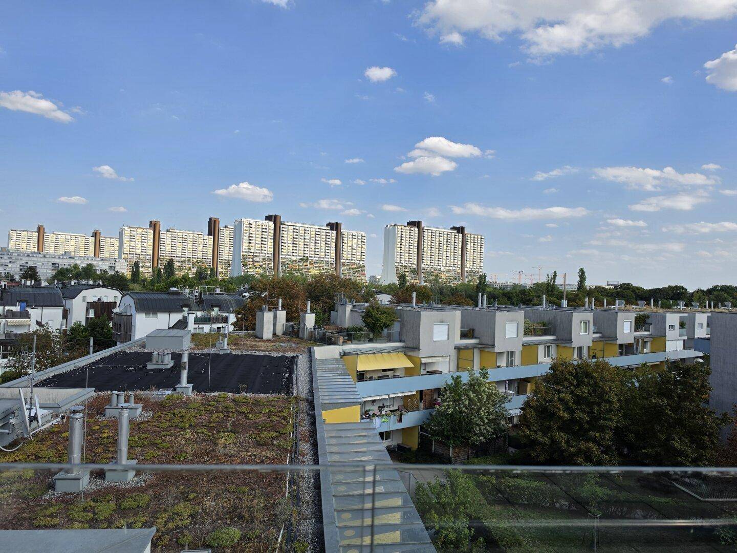 Panoramablick über Wohngebäude, grüne Dächer und die städtische Umgebung unter klarem Himmel.