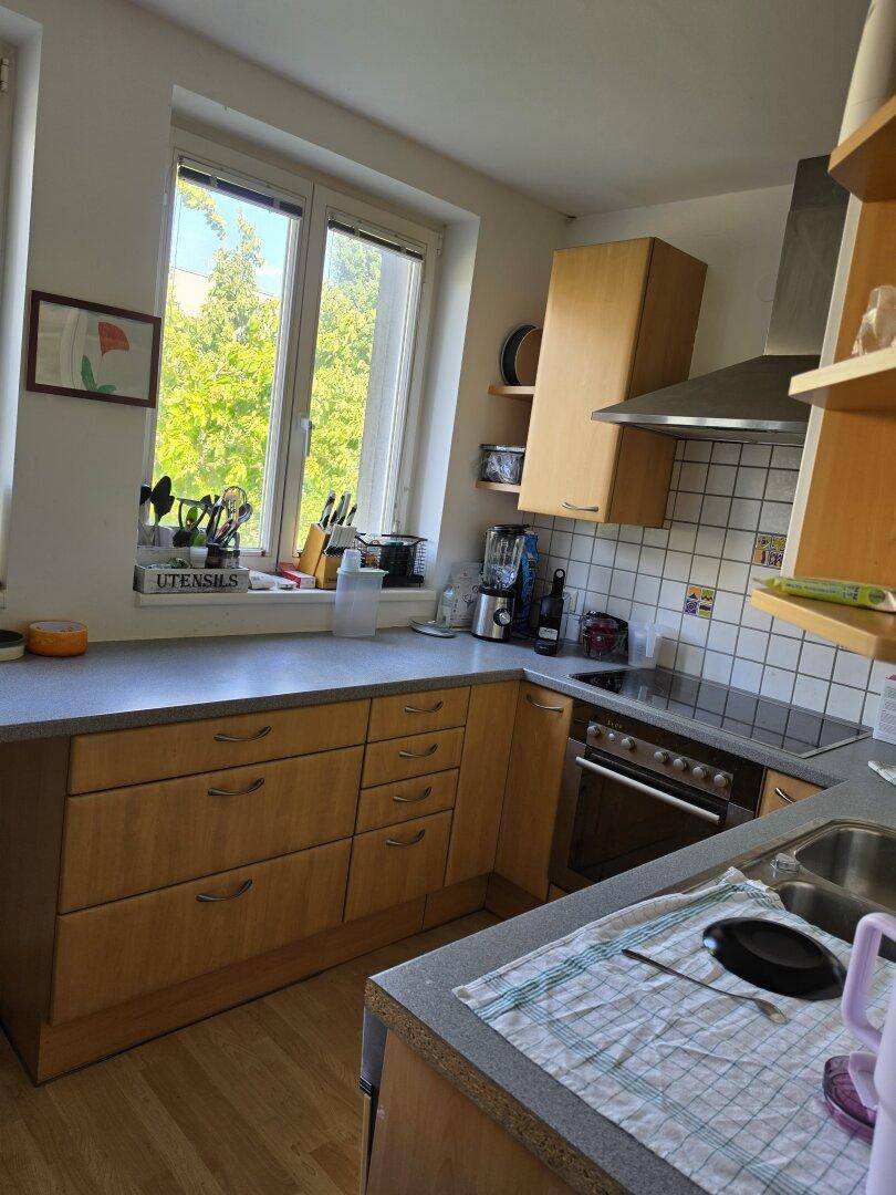 Funktionale Küche mit Holzelementen, Herd, Spüle und Dunstabzugshaube neben einem Fenster.