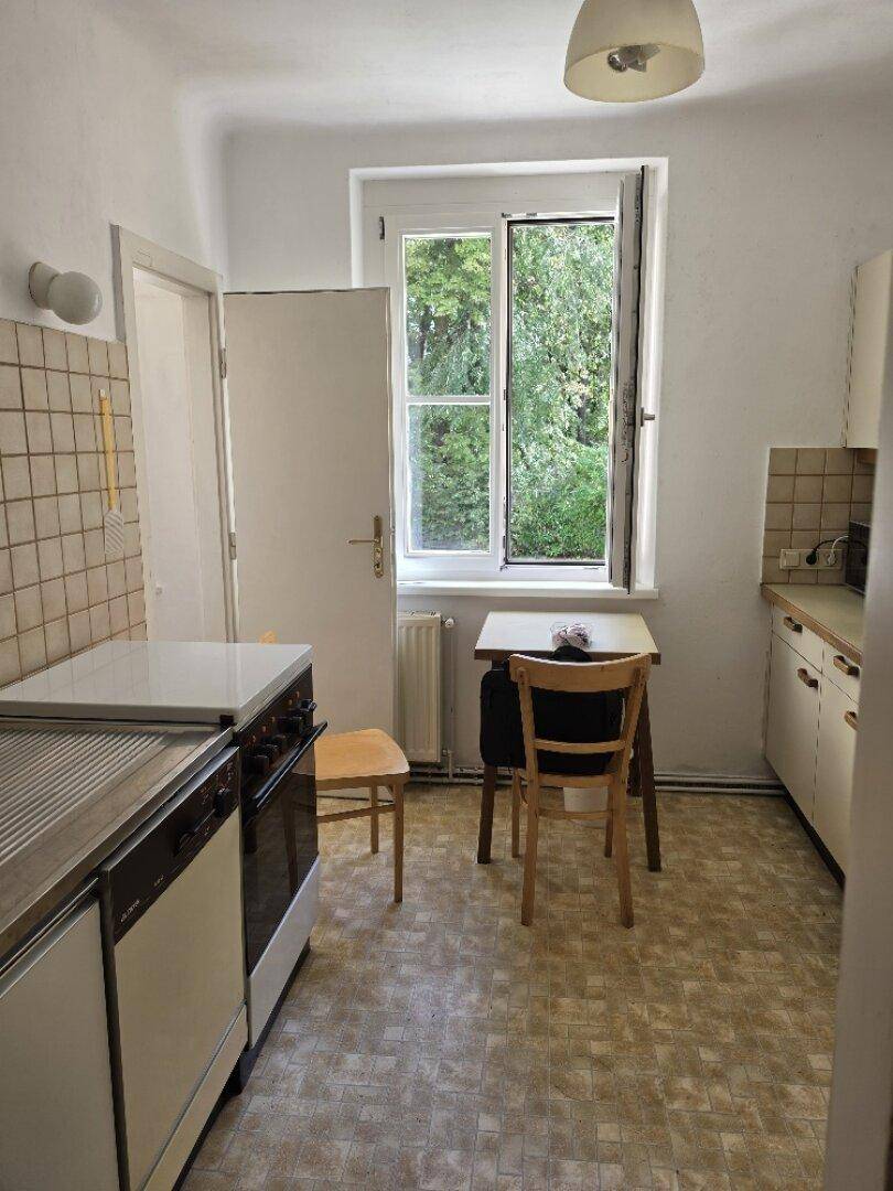 Funktionale Küche mit älteren Einbaumöbeln, Essbereich und Fenster mit Blick ins Grüne.