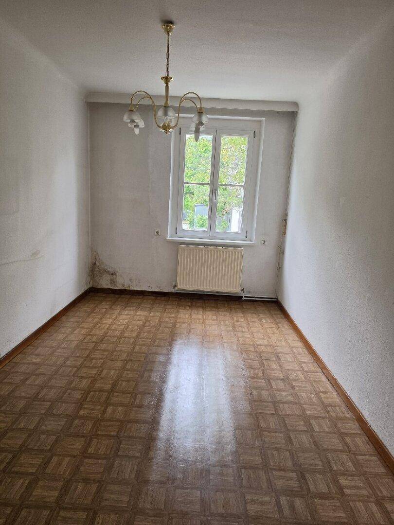 Helles Zimmer mit Parkettboden und großem Fenster, das viel Tageslicht hereinlässt.