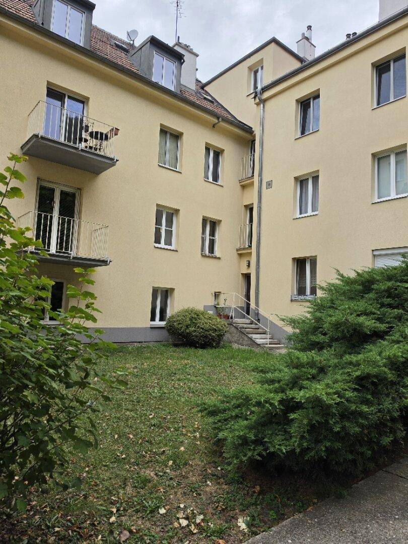 Außenansicht eines Mehrfamilienhauses mit gepflegtem Gemeinschaftsgarten und Balkonen.