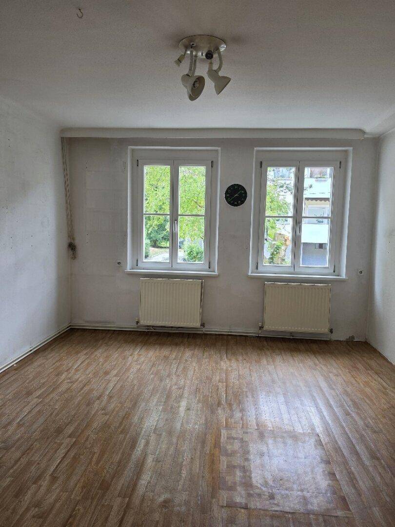 Geräumiges Zimmer mit zwei Fenstern und Parkettboden, bietet viel natürliches Licht und Grünblick.