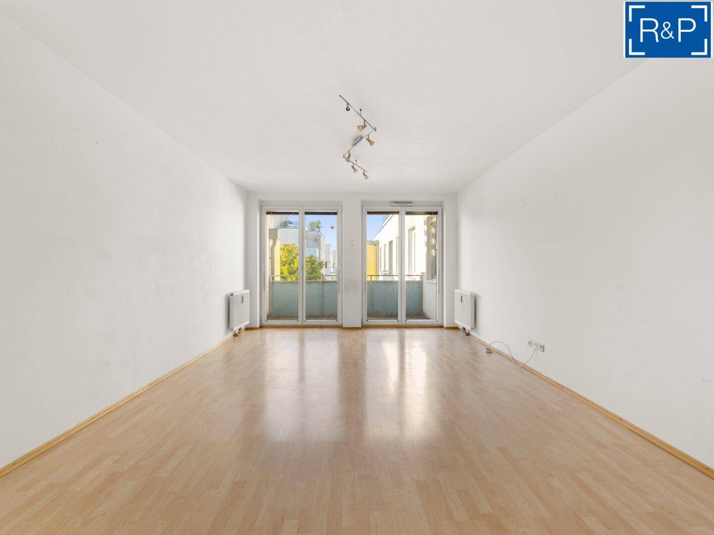 Geräumiges Wohnzimmer mit hellem Laminatboden und Zugang zu einem Balkon.