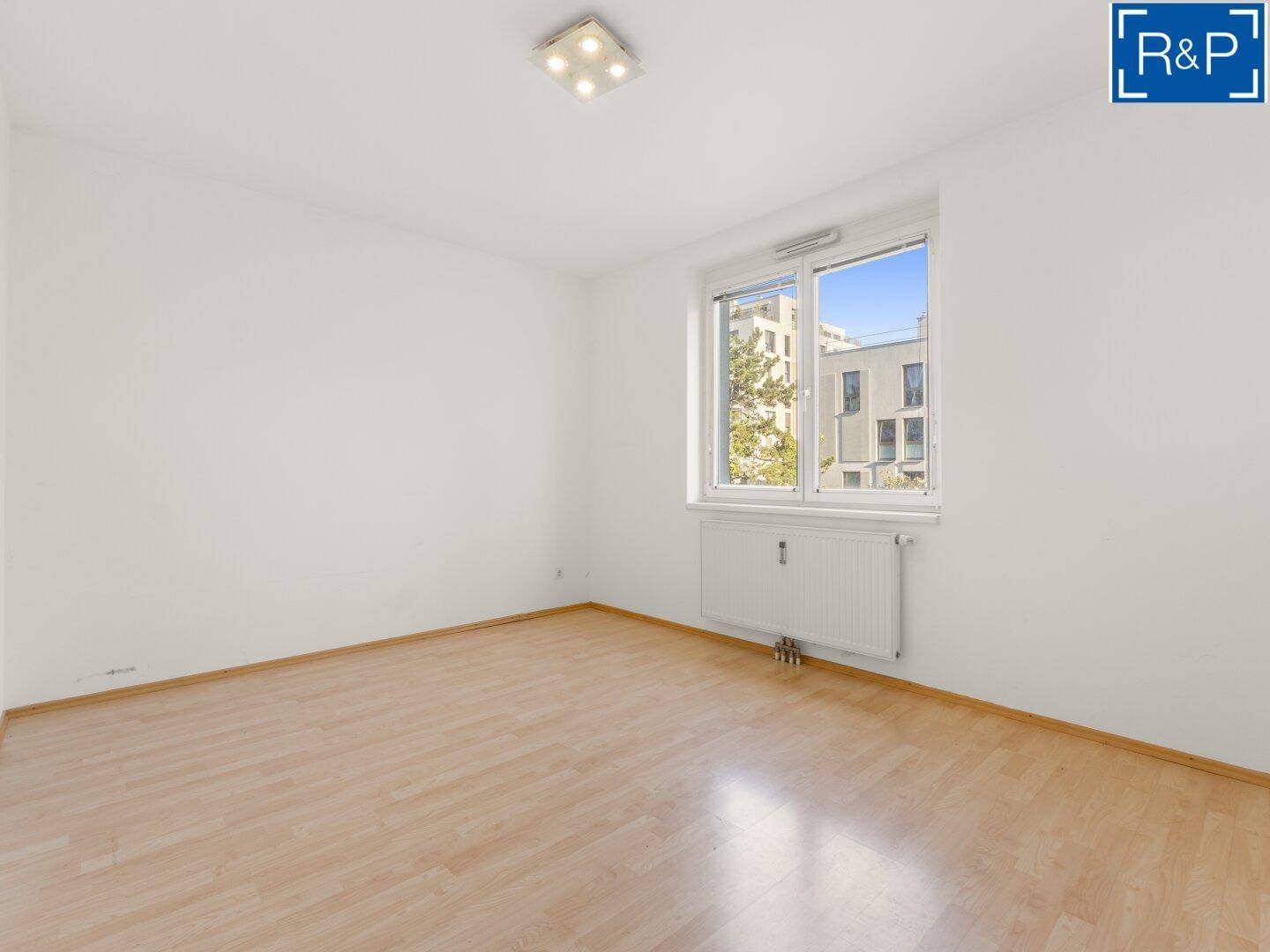 Helles Schlafzimmer mit Laminatboden und großem Fenster mit Blick ins Grüne.