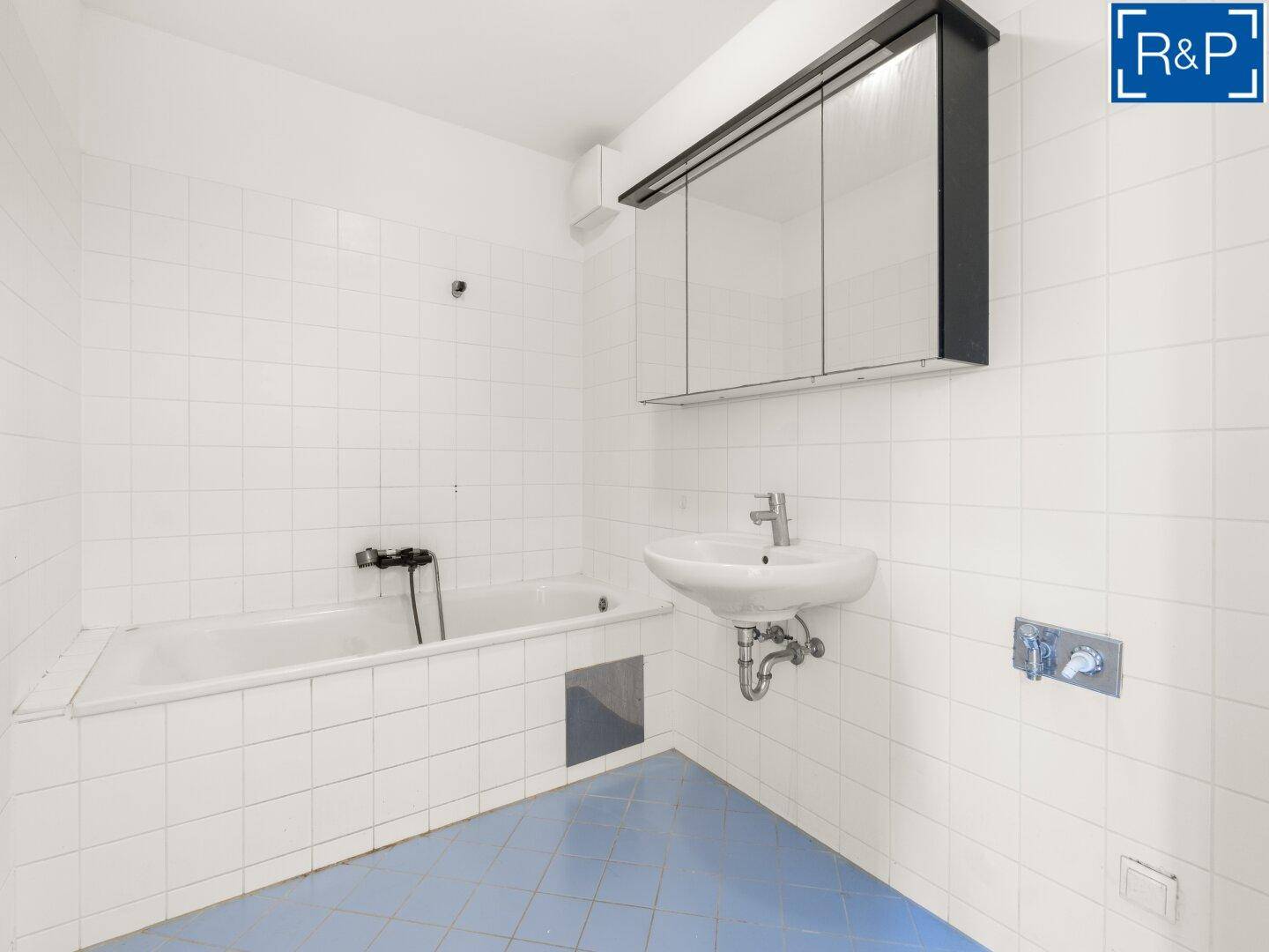 Badezimmer mit Badewanne, Waschbecken und Spiegelschrank, gefliest in Weiß und Blau.