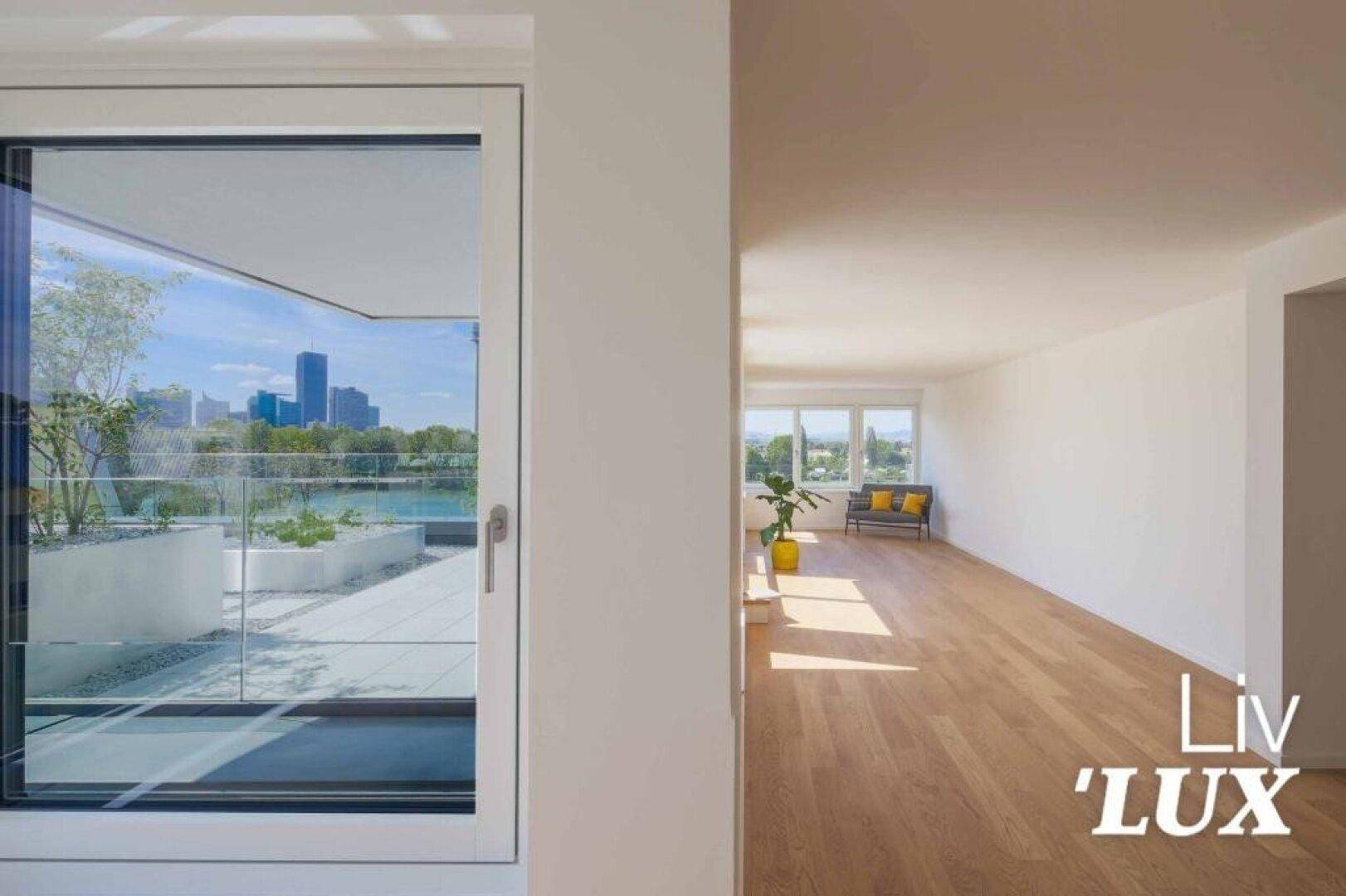 Heller Wohnbereich mit Holzboden und Blick durch große Fenster auf die Terrasse und Stadt.