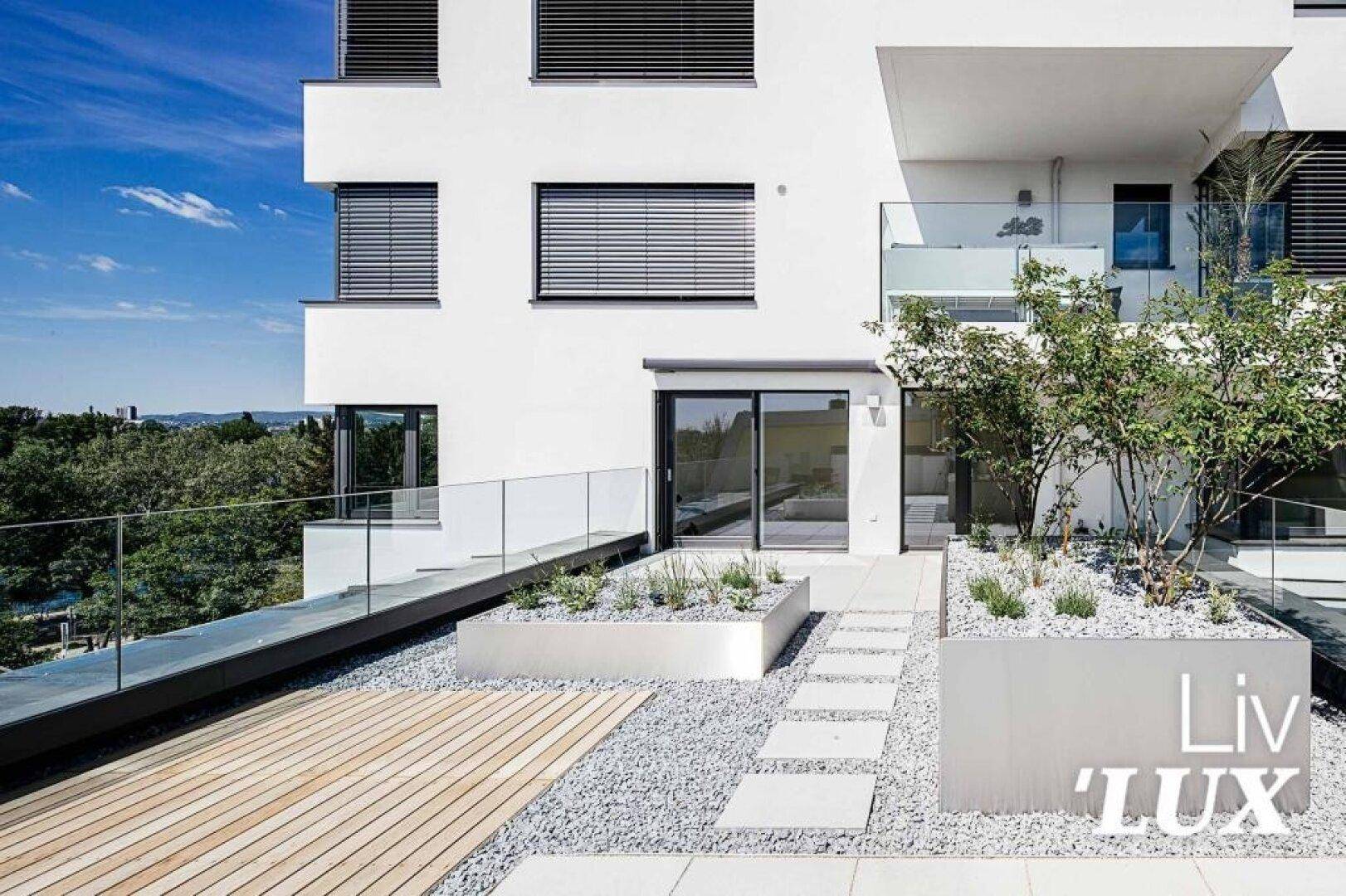 Moderne Terrasse mit Holz- und Kiesbereichen sowie Pflanzenbeeten am Gebäude.