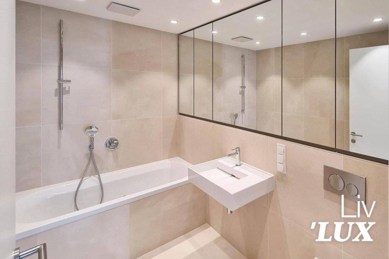 Modernes Badezimmer mit beigefarbenen Fliesen, Badewanne und Spiegelschrank.