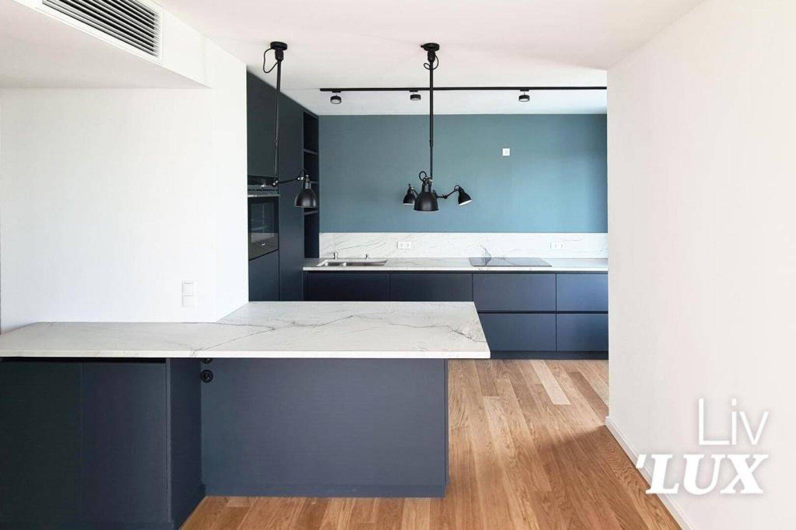 Offene, moderne Küche mit dunkelblauen Schränken, Marmorarbeitsplatten und Holzboden.