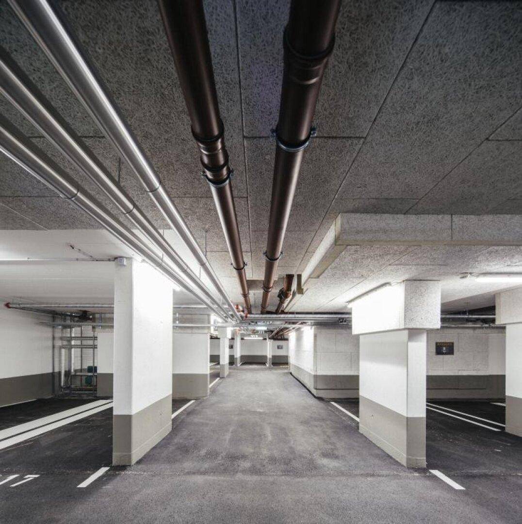 Tiefgarage mit sichtbaren Rohrleitungen an der Decke und Säulen.