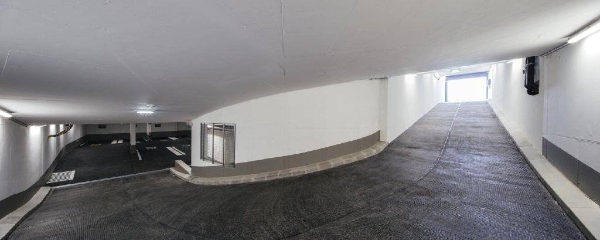 Einfahrt zur Tiefgarage mit breiter Rampe und guter Beleuchtung.