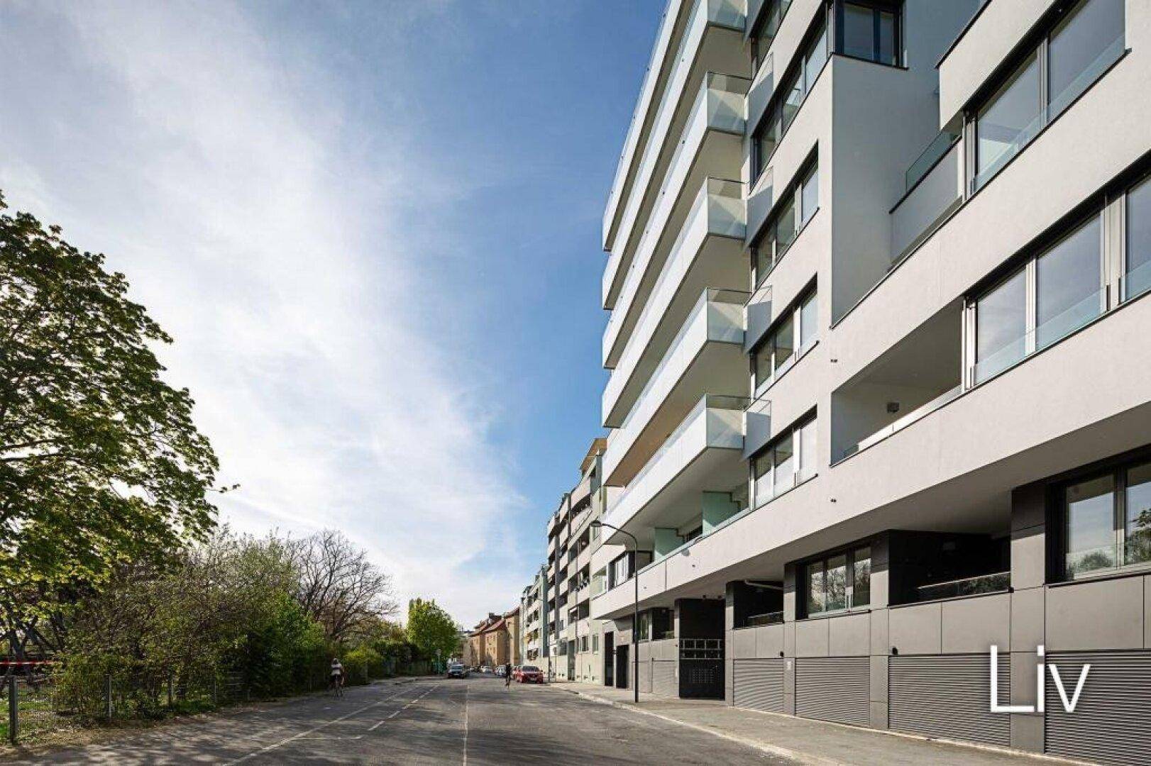 Moderne Wohngebäude-Fassade mit Balkonen und großen Fenstern an einer städtischen Straße.