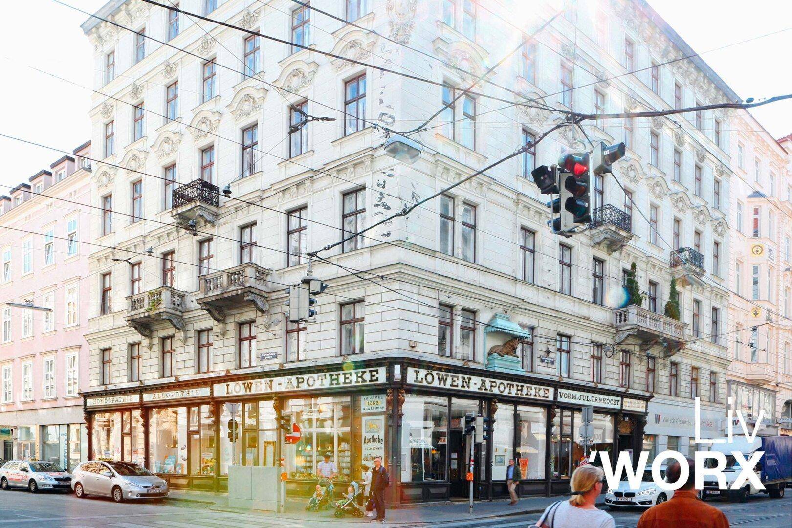 Historisches Eckgebäude mit Apotheke im Erdgeschoss, Balkonen und vielen Fenstern in der Stadt.