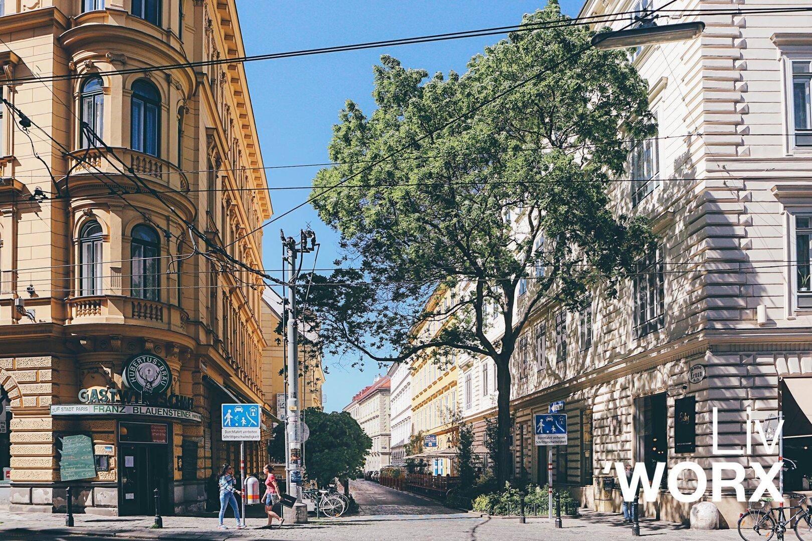 Malerische Stadtstraße mit alten Gebäuden, hohen Bäumen und sonnigem Wetter.