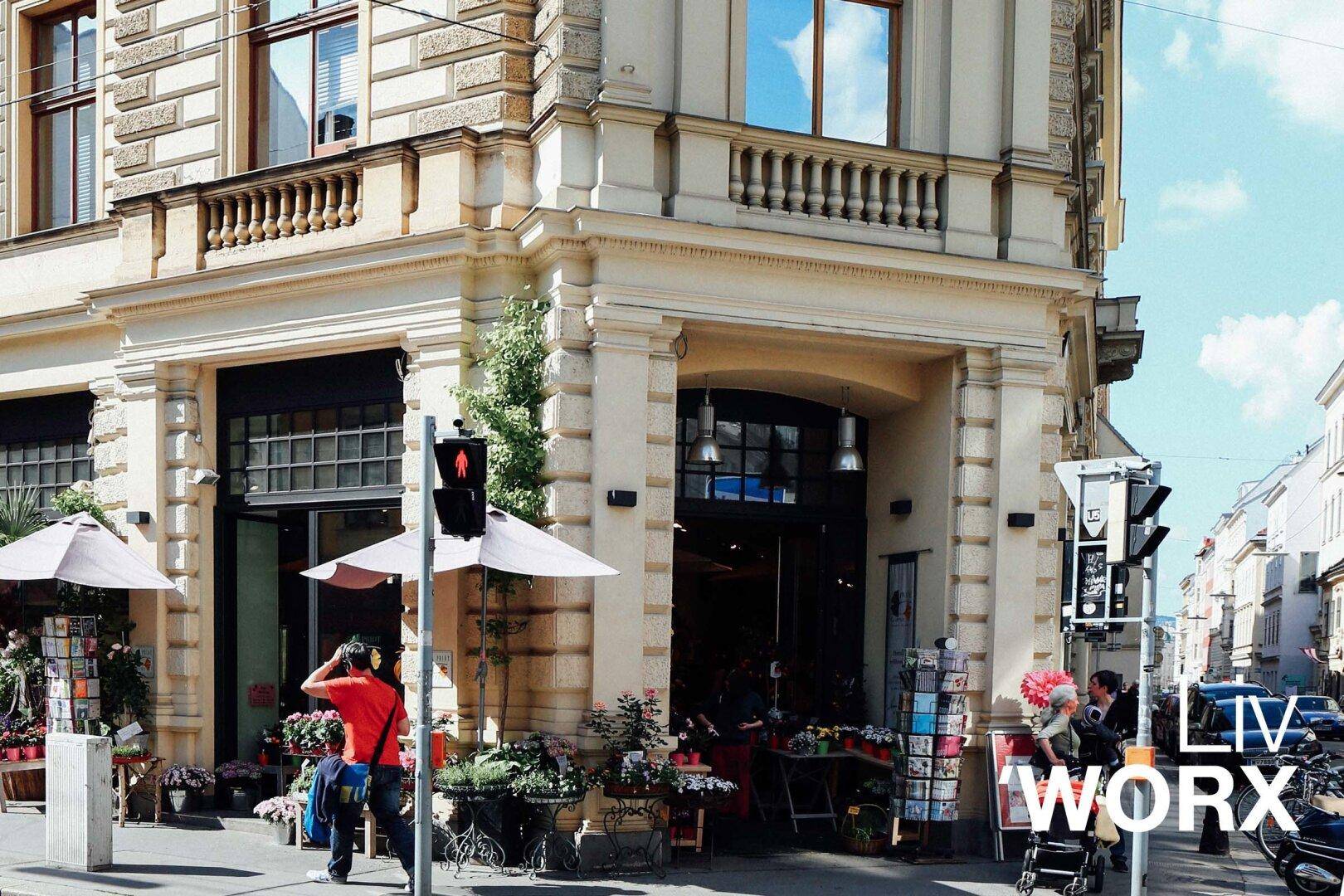 Belebtes Straßeneck mit einem Blumengeschäft im Erdgeschoss und klassischer Architektur.