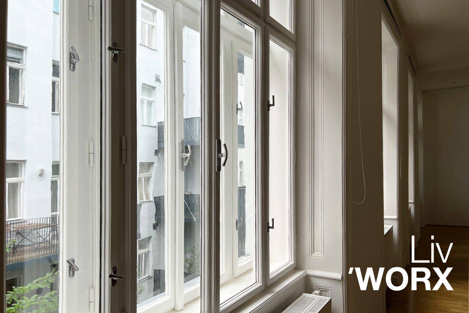 Große, weiße Fenster mit Blick auf einen Innenhof und gegenüberliegende Gebäude.