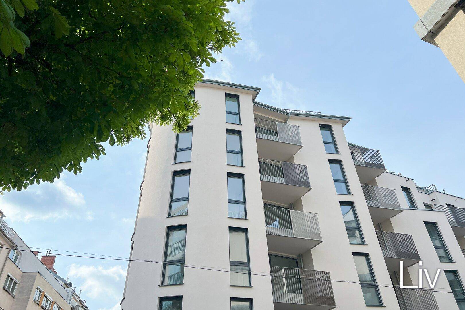 Modernes Wohngebäude mit heller Fassade und zahlreichen Balkonen unter blauem Himmel.