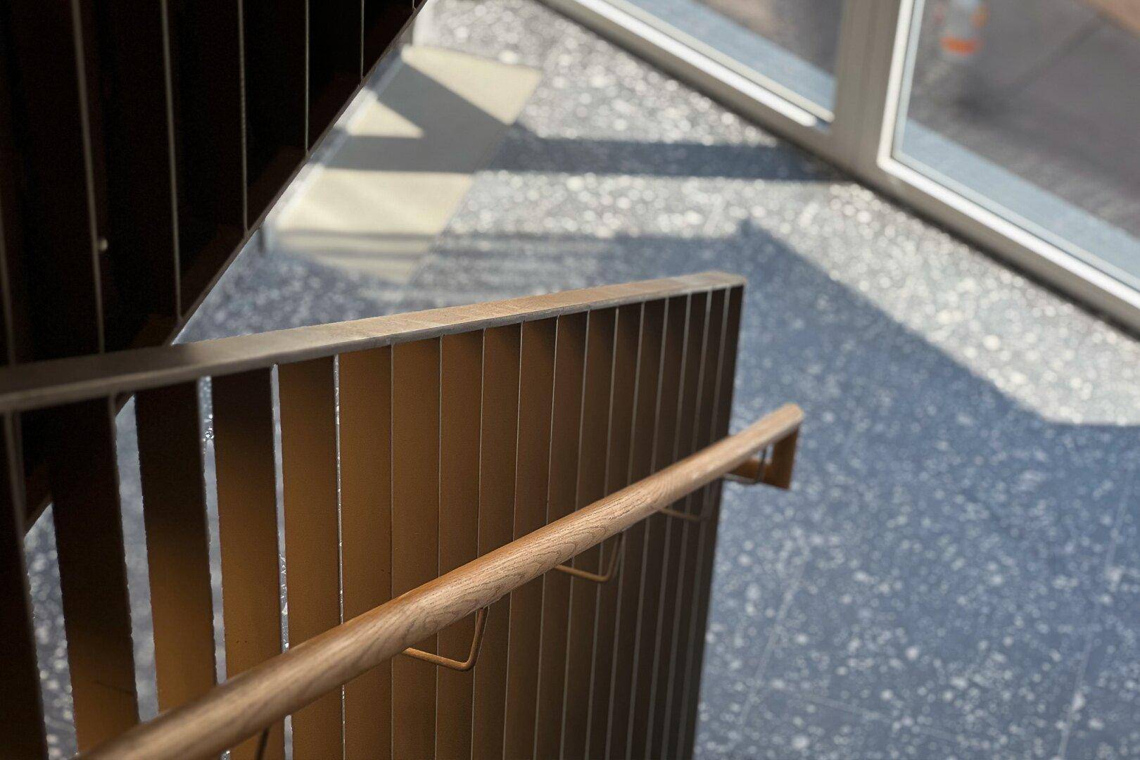 Modernes Treppenhaus mit Metallgeländer und Terrazzoboden, gut beleuchtet durch ein Fenster.