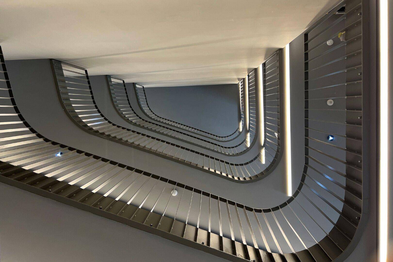 Modernes Treppenhaus mit elegantem Metallgeländer und integrierter Beleuchtung, von unten nach oben fotografiert.