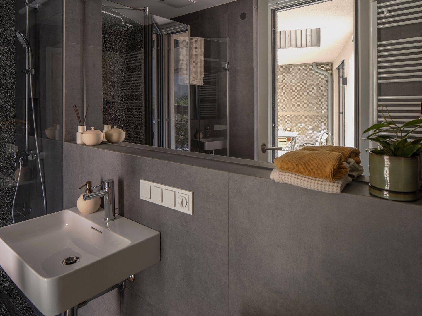 Modernes Badezimmer mit grauen Fliesen, Einzelwaschbecken und Blick nach draußen.