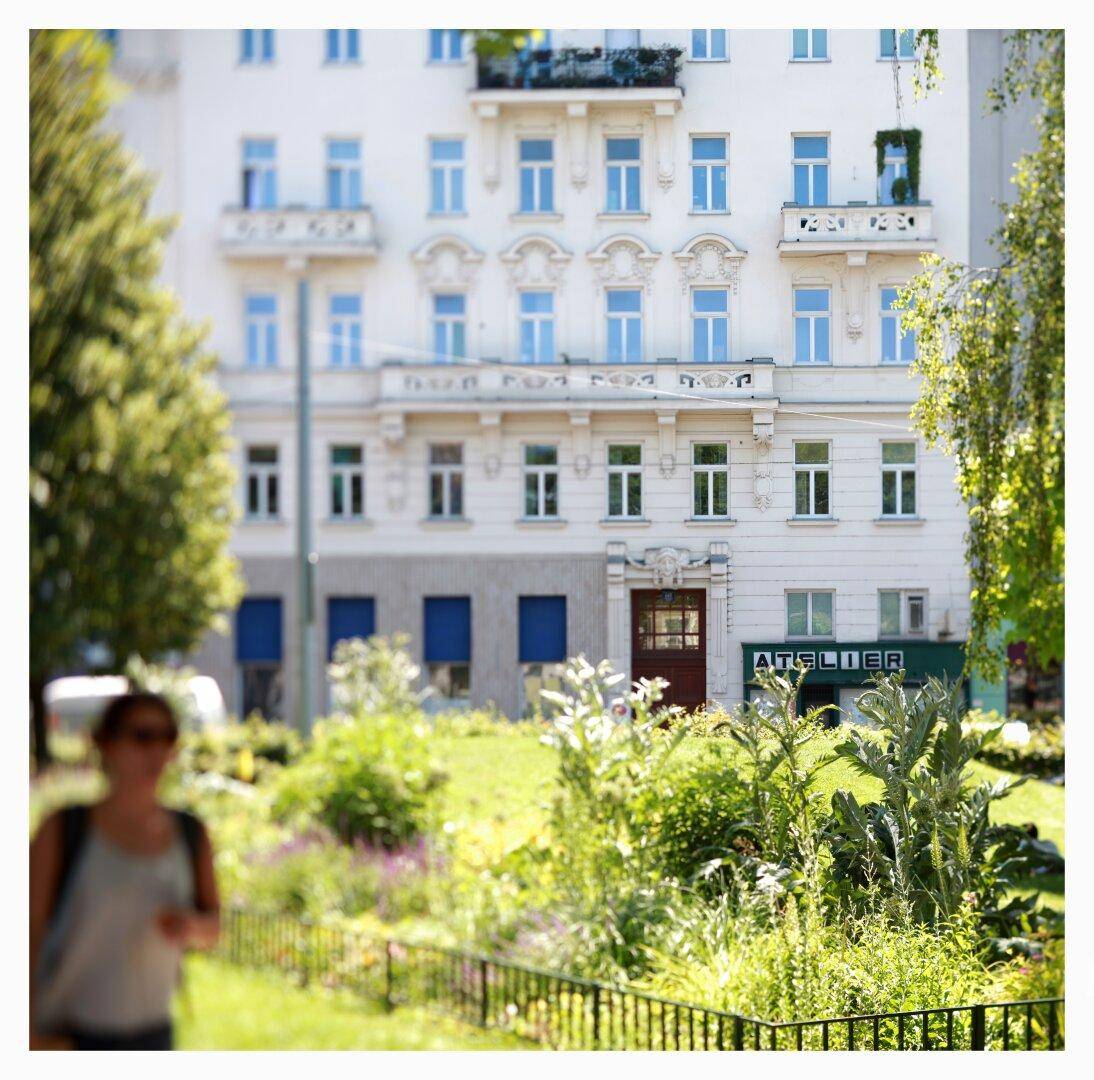 Eine klassische Gebäudefassade hinter einem gepflegten Gartenbereich mit üppiger Bepflanzung.