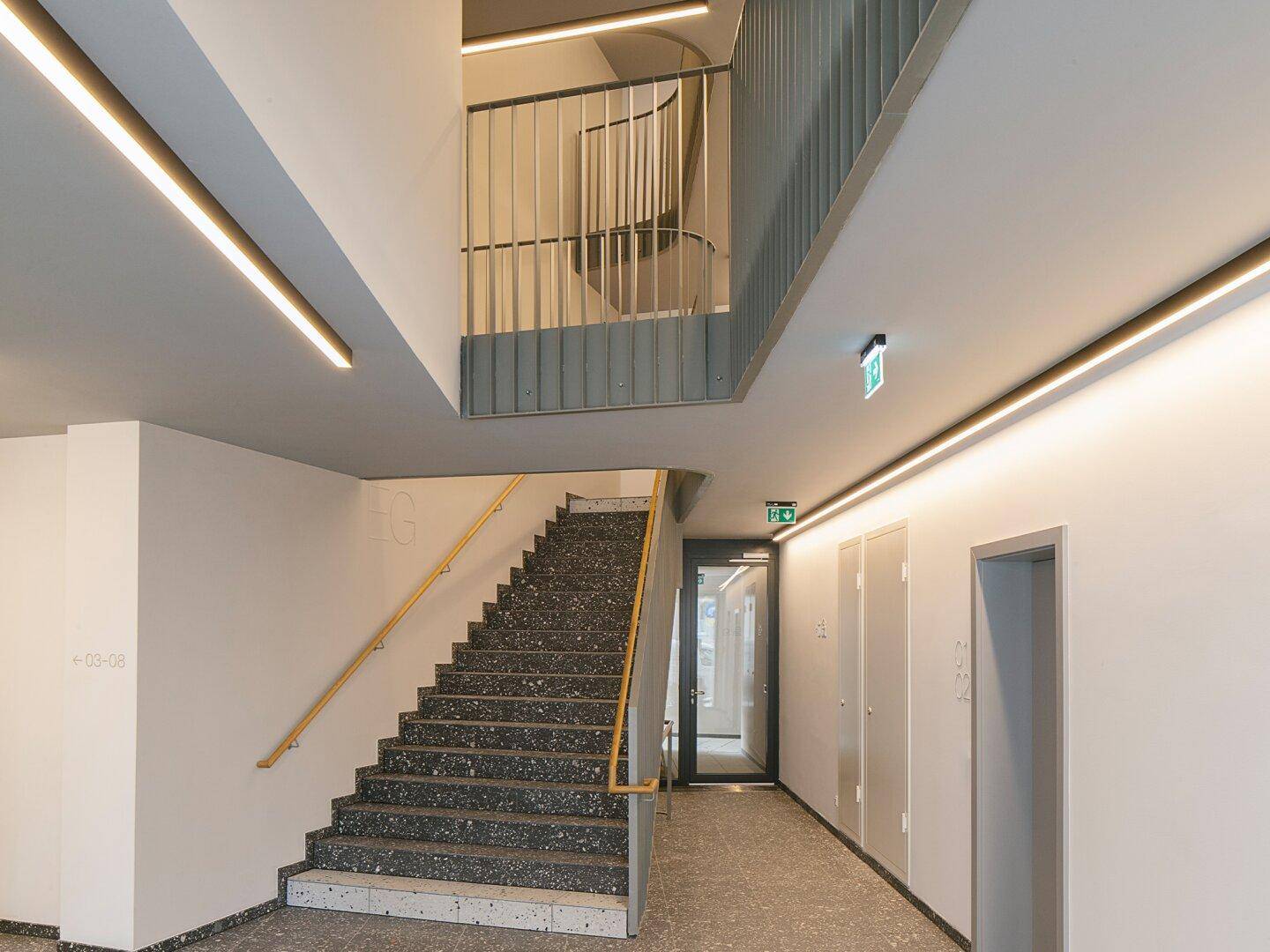 Helles Treppenhaus mit modernem Terrazzoboden und indirekter Beleuchtung in einem Neubau.