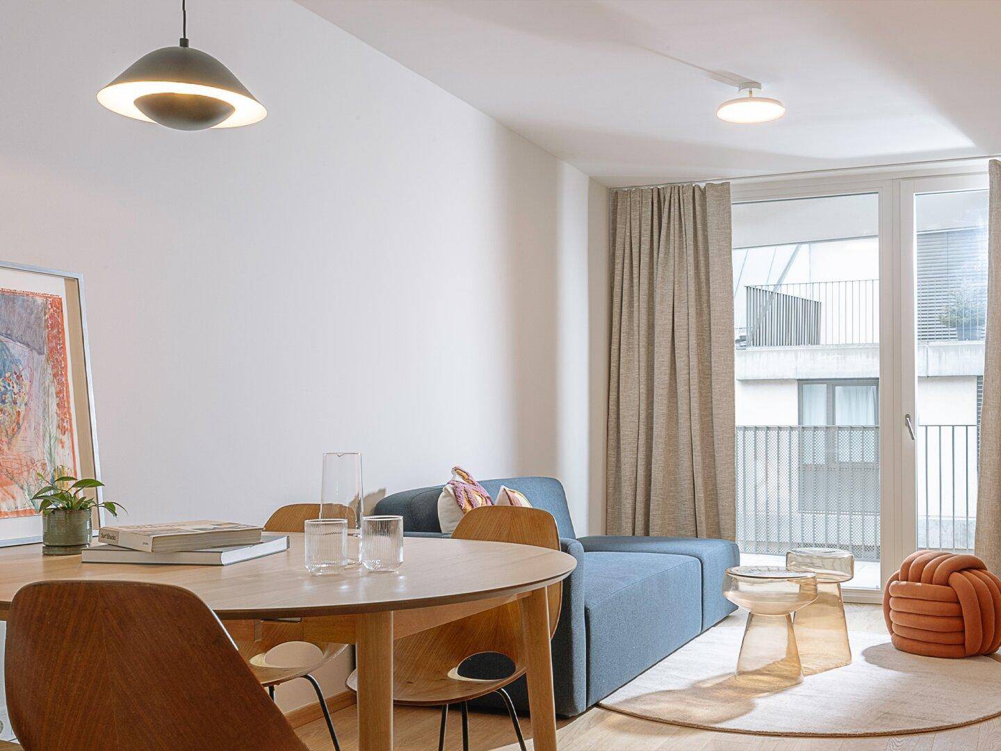 Offener Wohn- und Essbereich mit modernem Esstisch, Sofa und Zugang zu einem Balkon.