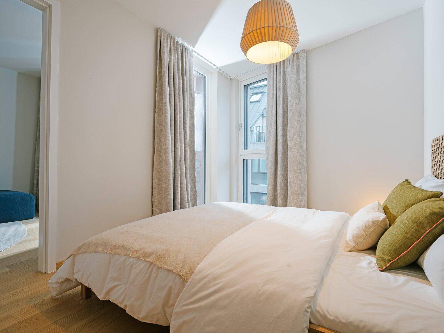 Gemütliches Schlafzimmer mit großem Bett, Holzboden und Fenster mit Blick auf die umliegenden Gebäude.