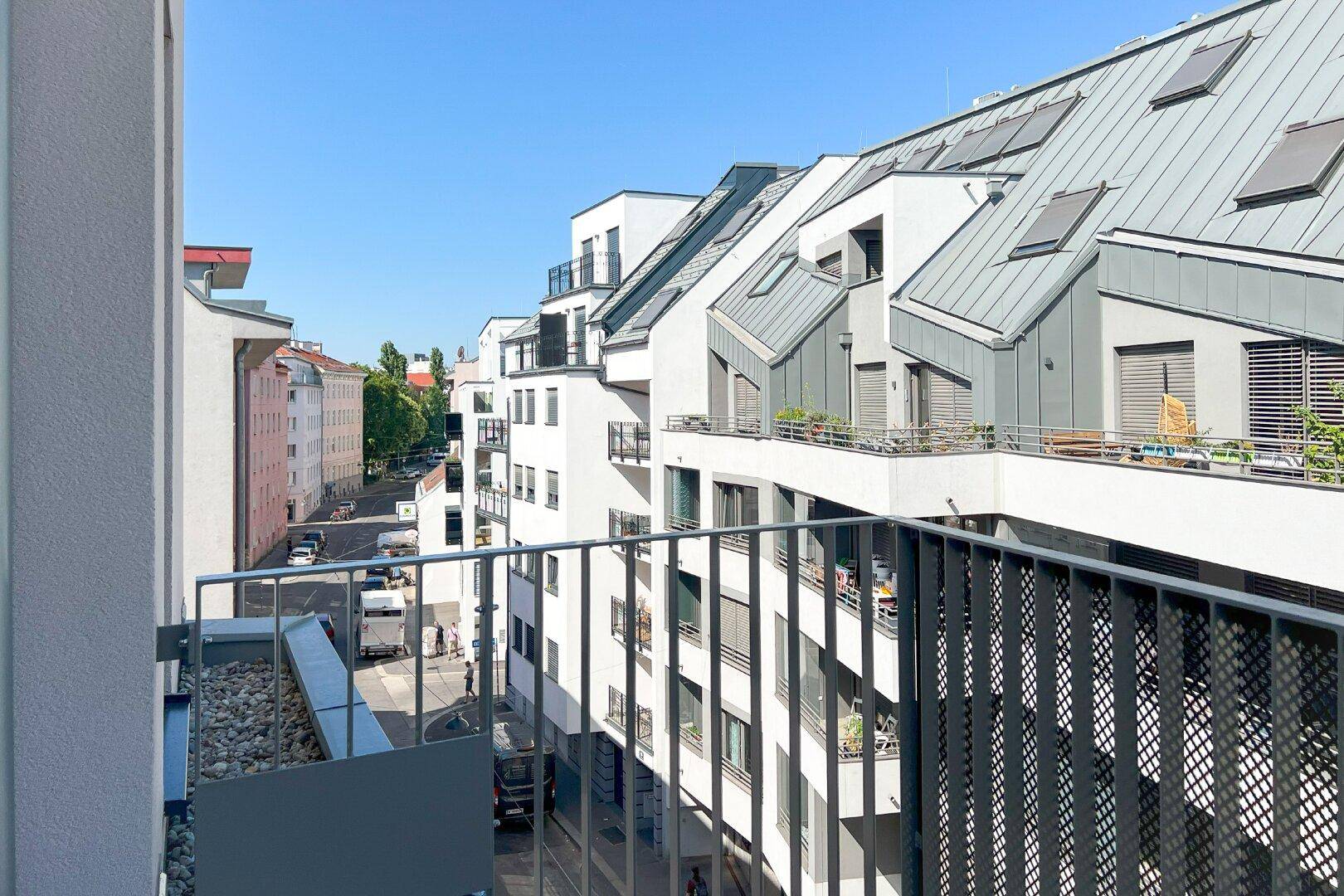 Blick von einem Balkon auf eine belebte Straße und moderne Gebäude mit vielen Fenstern und Dachschrägen.