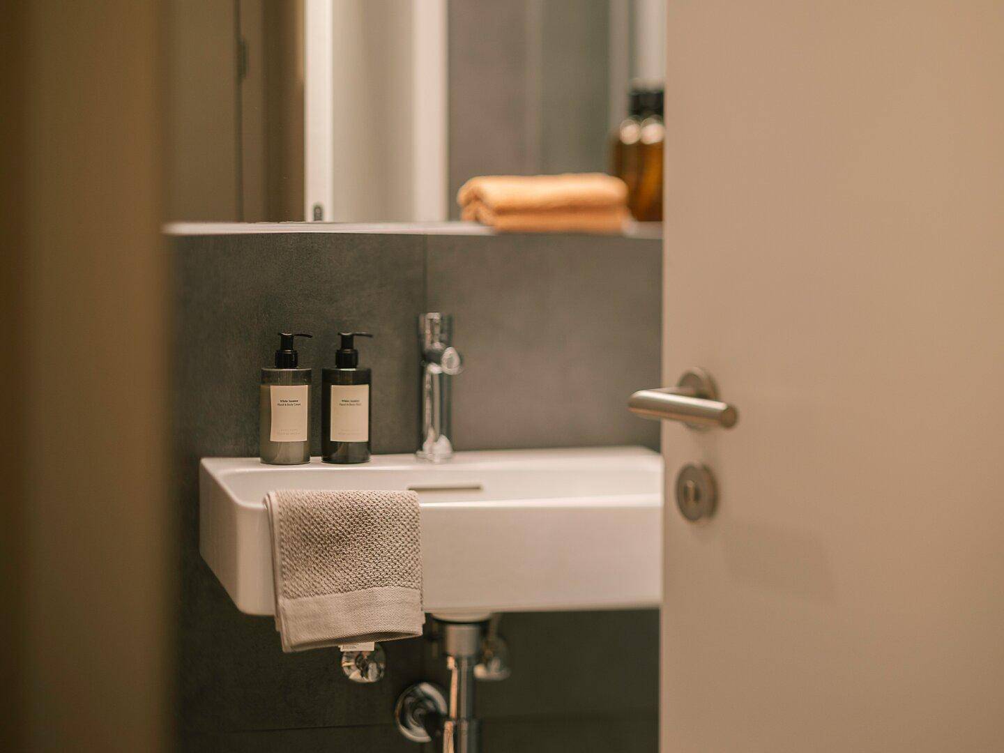 Modernes Badezimmer mit elegantem Waschbecken, Spiegel und dunklen Fliesen an der Wand.