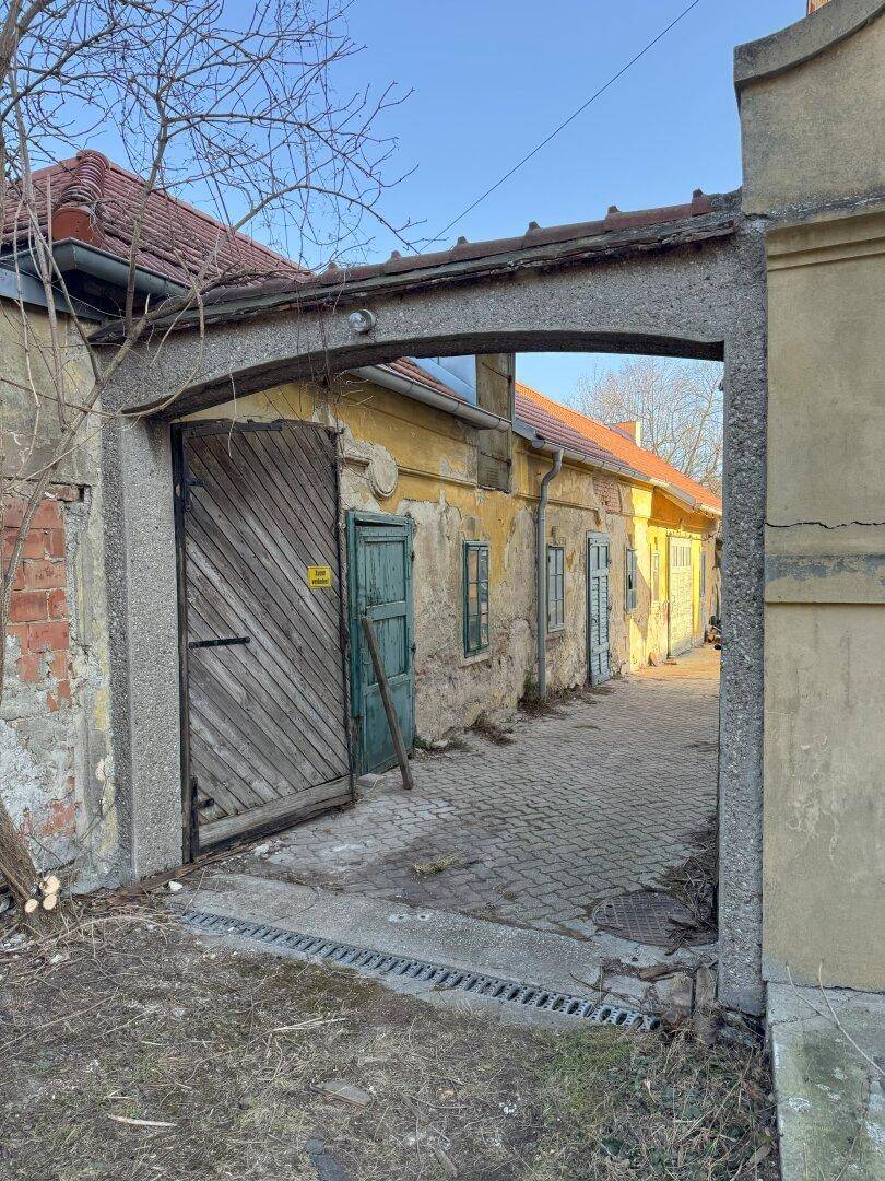 Historischer Torbogen führt zu einem gepflasterten Innenhof mit alten, charmanten Gebäuden.