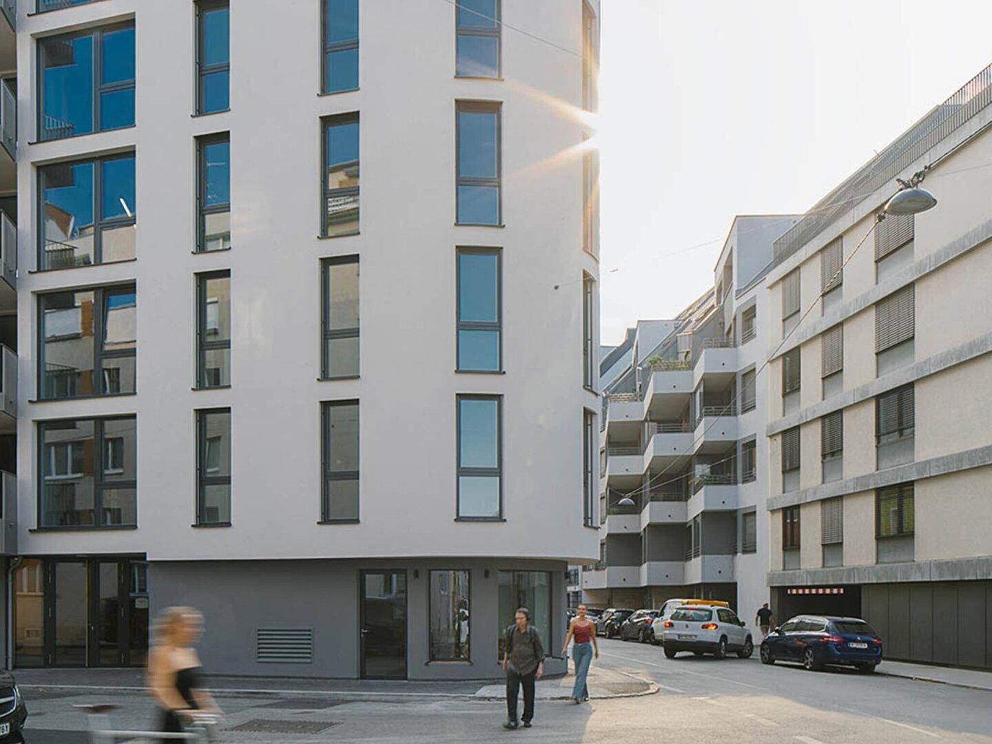 Modernes Wohngebäude mit großen Fenstern und Balkonen an einer städtischen Straße bei Tageslicht.