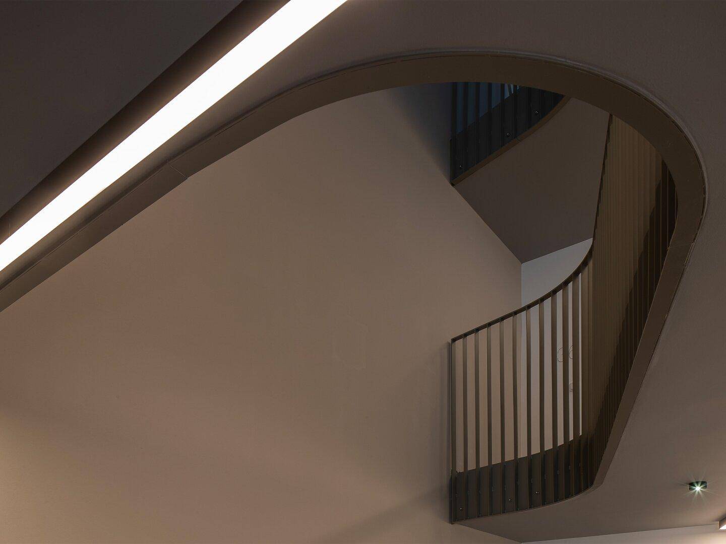 Moderne geschwungene Treppe in einem Gebäude mit indirekter Deckenbeleuchtung.