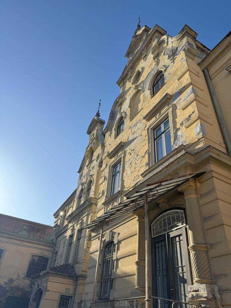 Herrschaftliches Gebäude mit abblätterndem Putz und hohen Fenstern unter strahlend blauem Himmel.