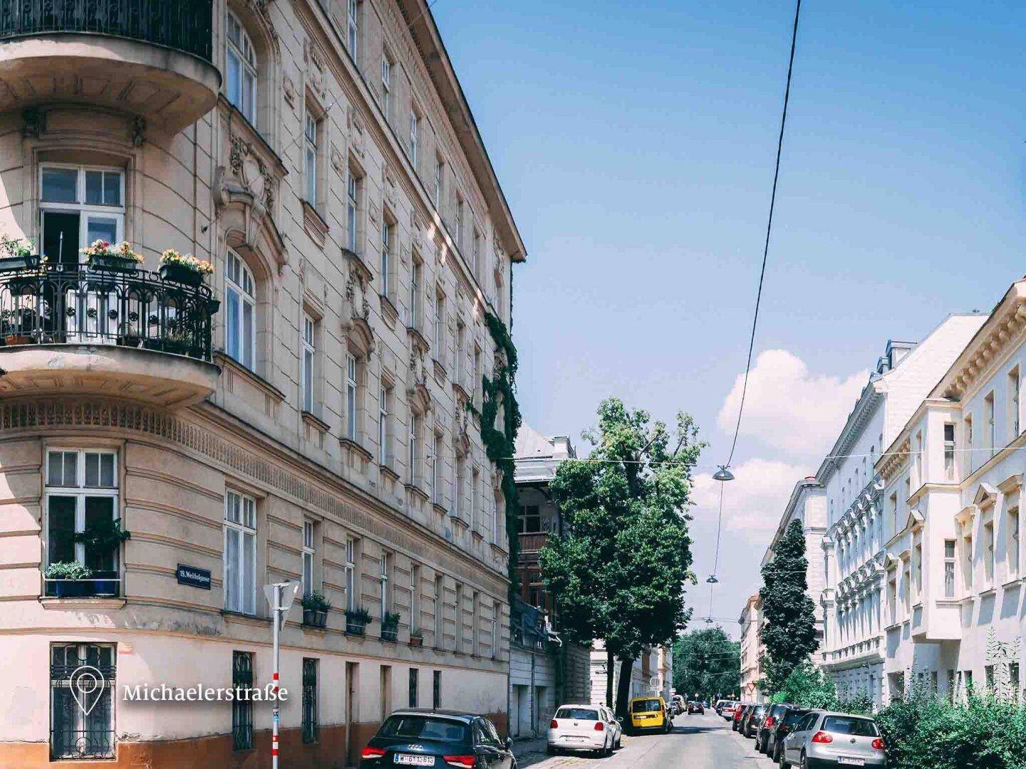 Straßenansicht eines klassischen Gebäudes mit traditionellem Balkon und parkenden Autos.