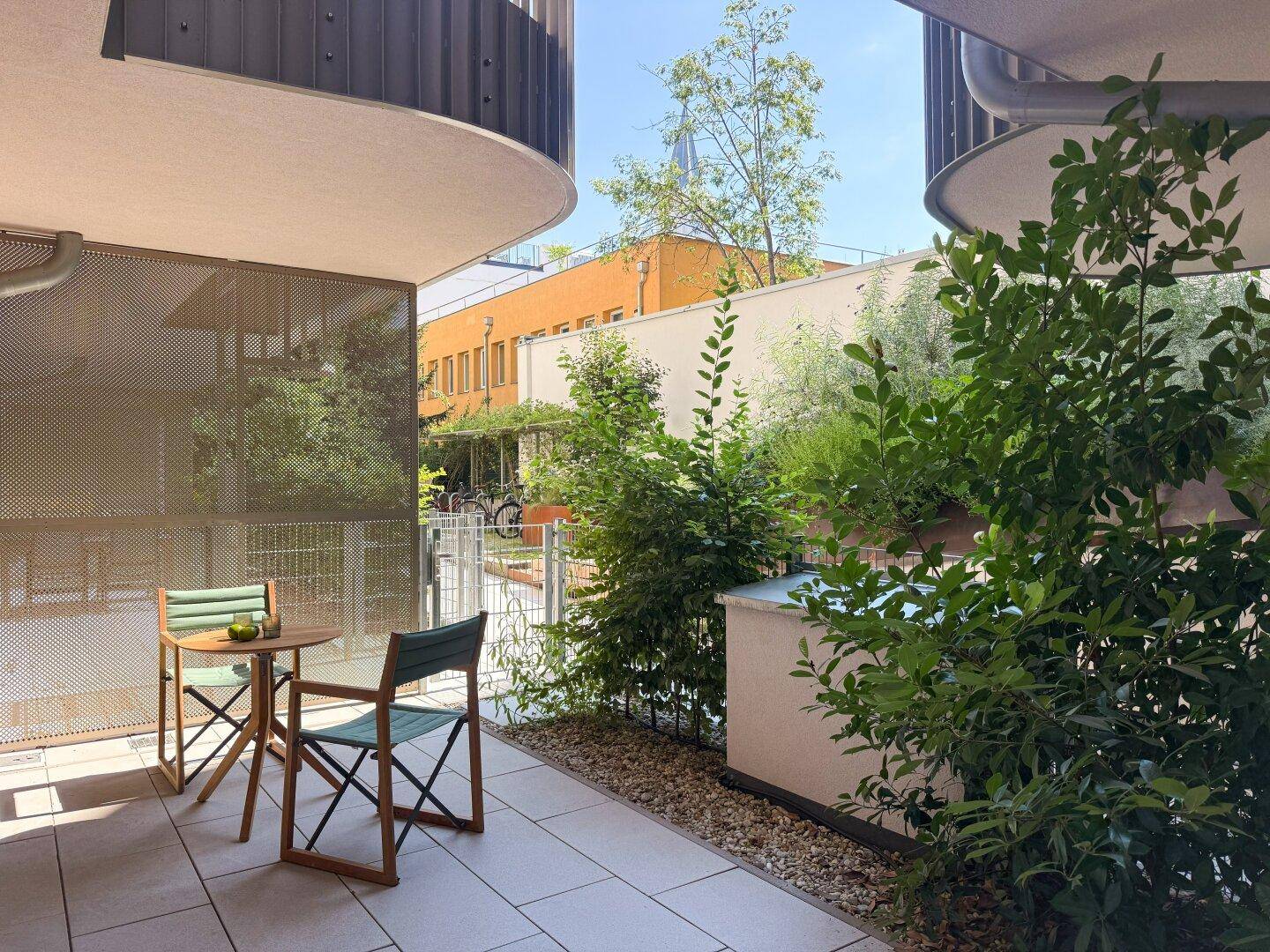 Gemütliche Terrasse mit Sitzgelegenheiten und viel Grün in einer ruhigen Wohnanlage.