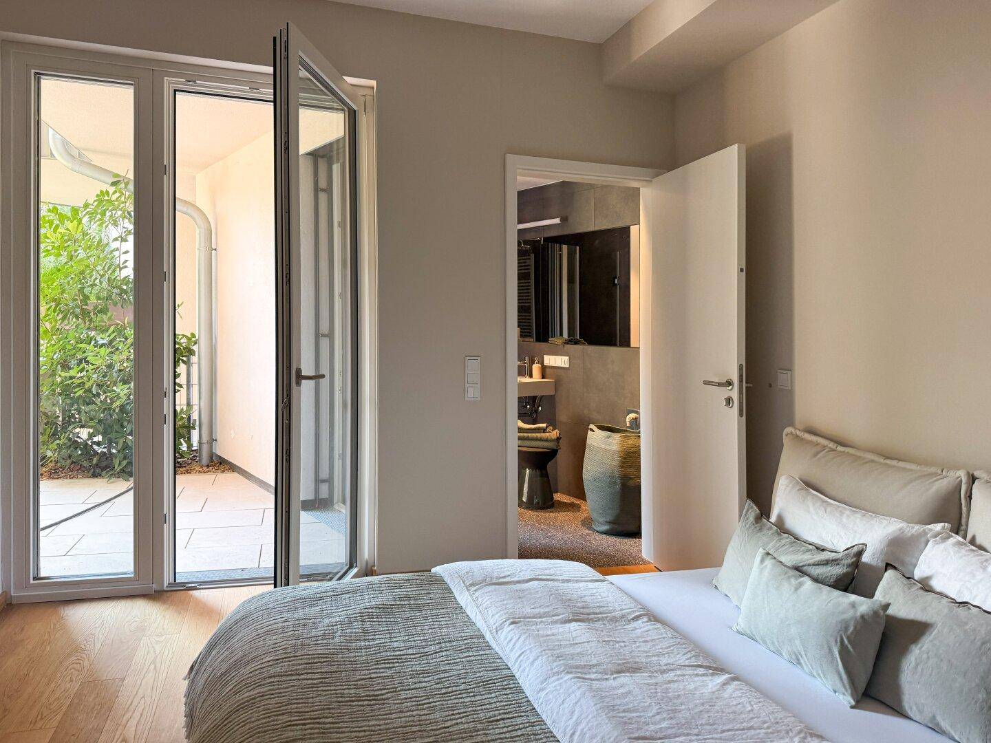 Schlafzimmer mit Holzboden, Zugang zum Badezimmer und Blick auf den Außenbereich.