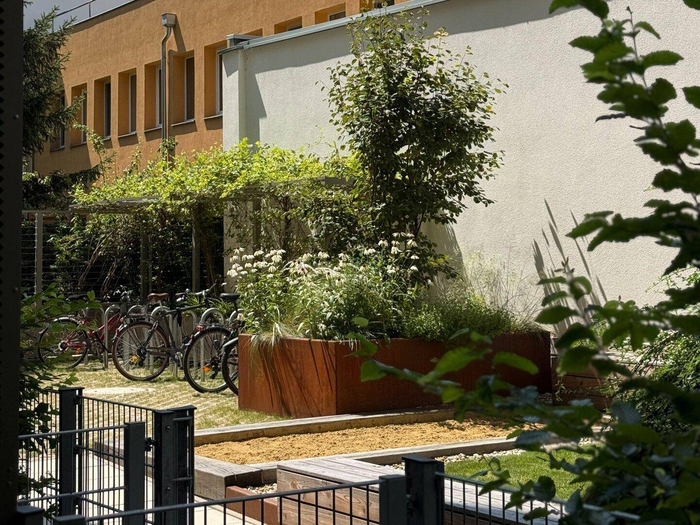 Begrünter Außenbereich mit Blumenbeeten, Bäumen und Fahrradständern in der Wohnanlage.