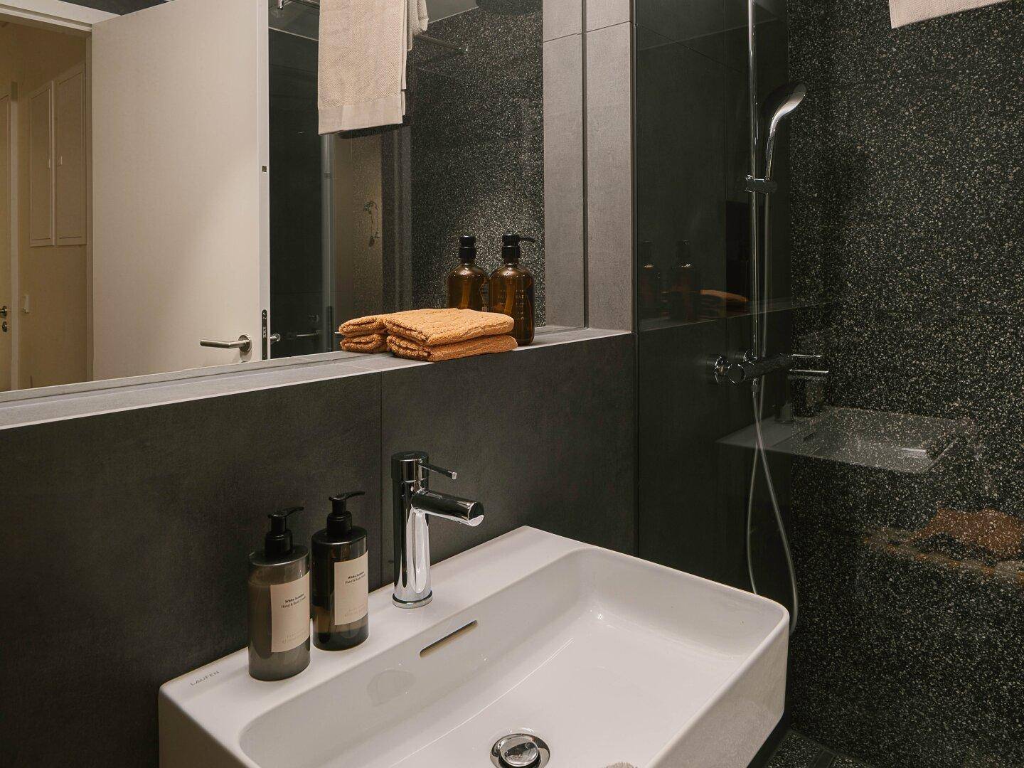 Modernes Badezimmer mit stilvollem Waschbecken, großem Spiegel und dunklen Fliesen.