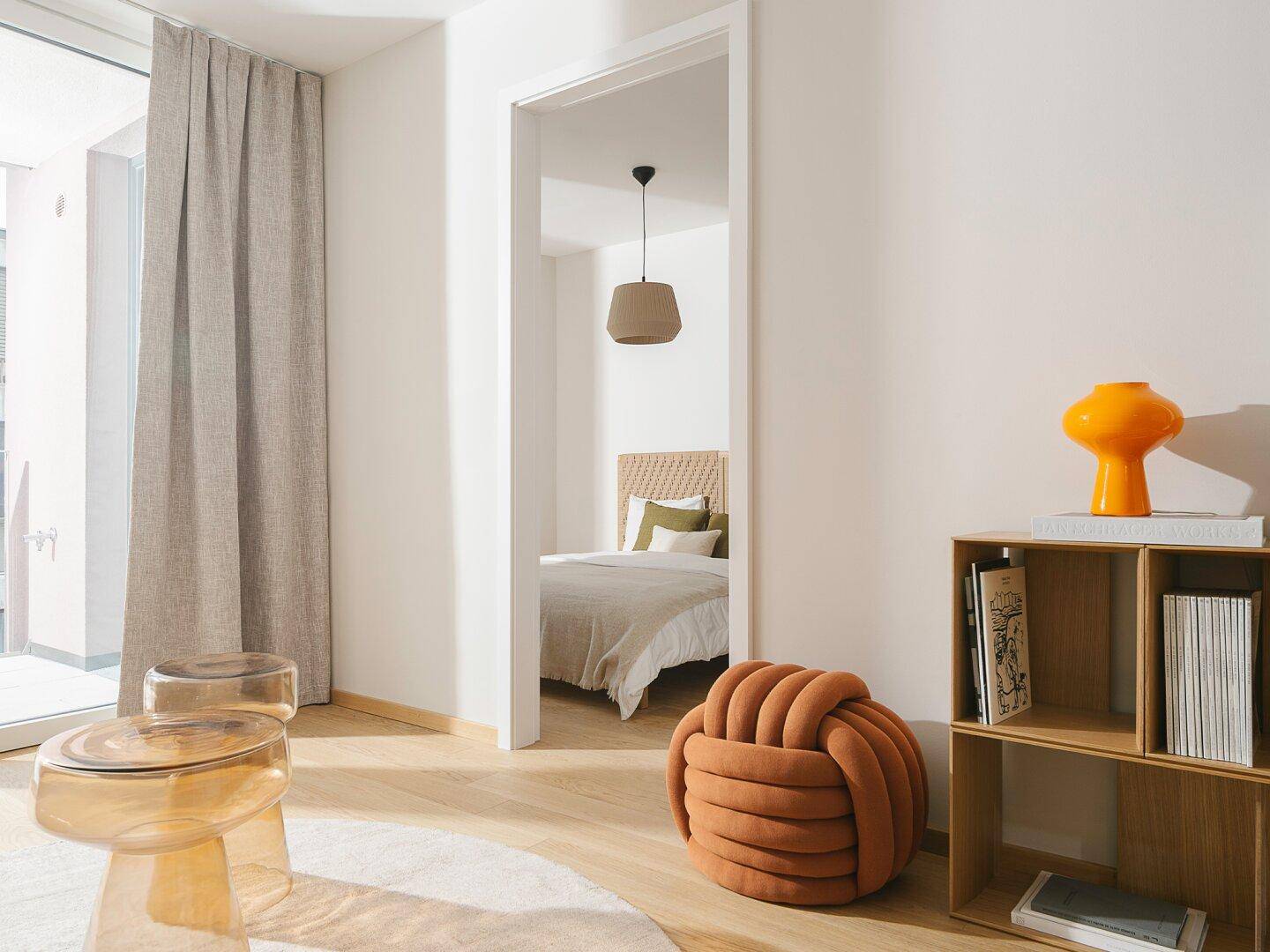 Blick vom Wohnbereich in ein gemütliches Schlafzimmer mit Rattan-Kopfteil und heller Einrichtung.