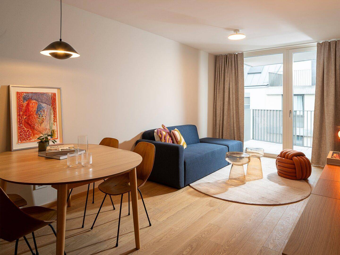 Helles Wohn- und Esszimmer mit modernem Sofa, Esstisch und Zugang zum Balkon.