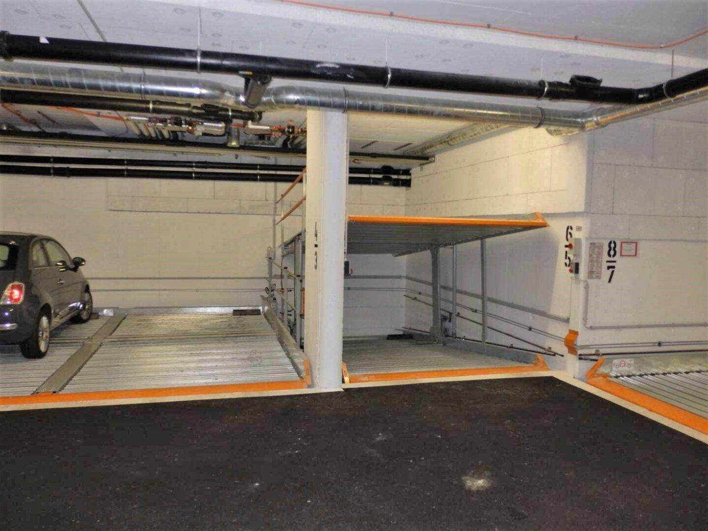 Tiefgarage mit mehreren Doppelparker-Systemen, eines davon mit einem geparkten Kleinwagen und freiem Stellplatz.