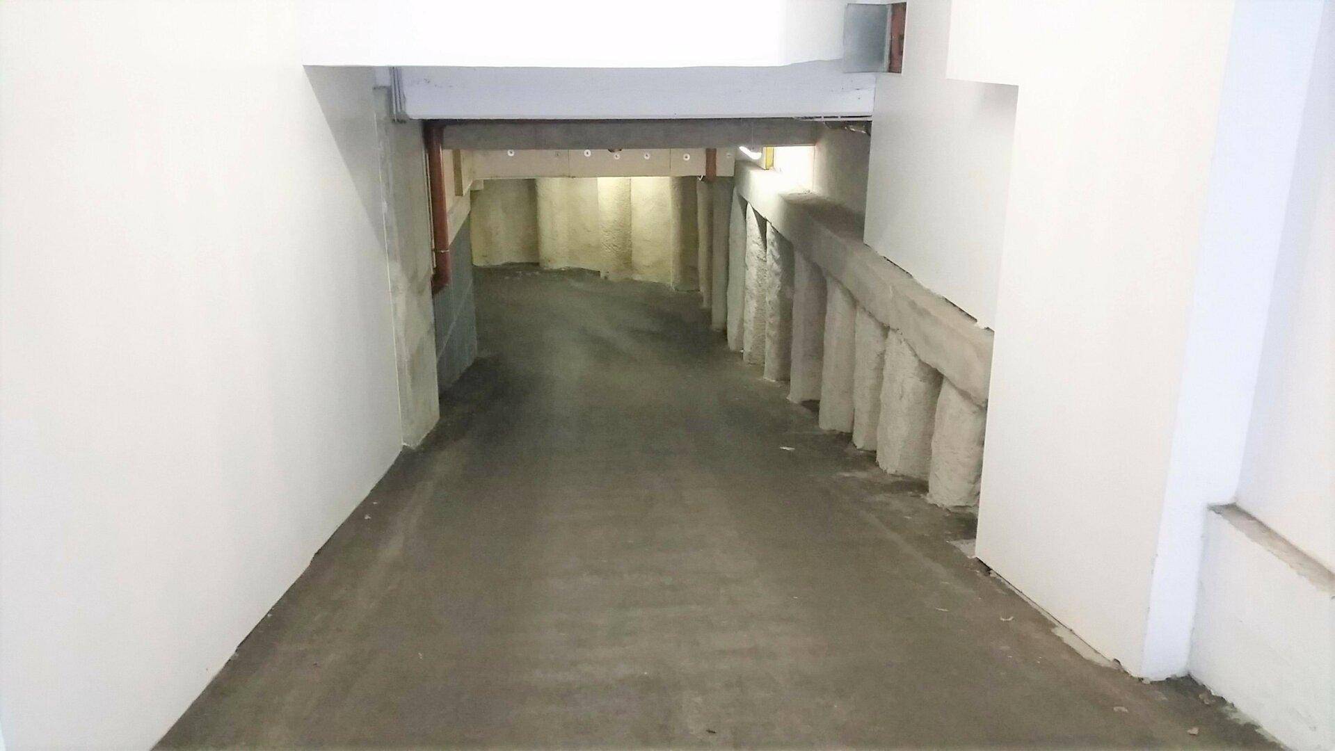 Einfahrt zu einer Tiefgarage mit einer abfallenden Rampe und robusten Betonwänden.