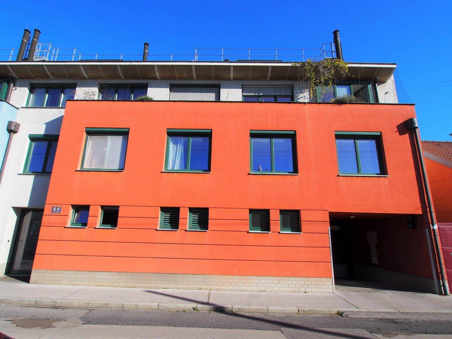 Modernes Gebäude mit auffälliger oranger Fassade und grünen Fensterrahmen.