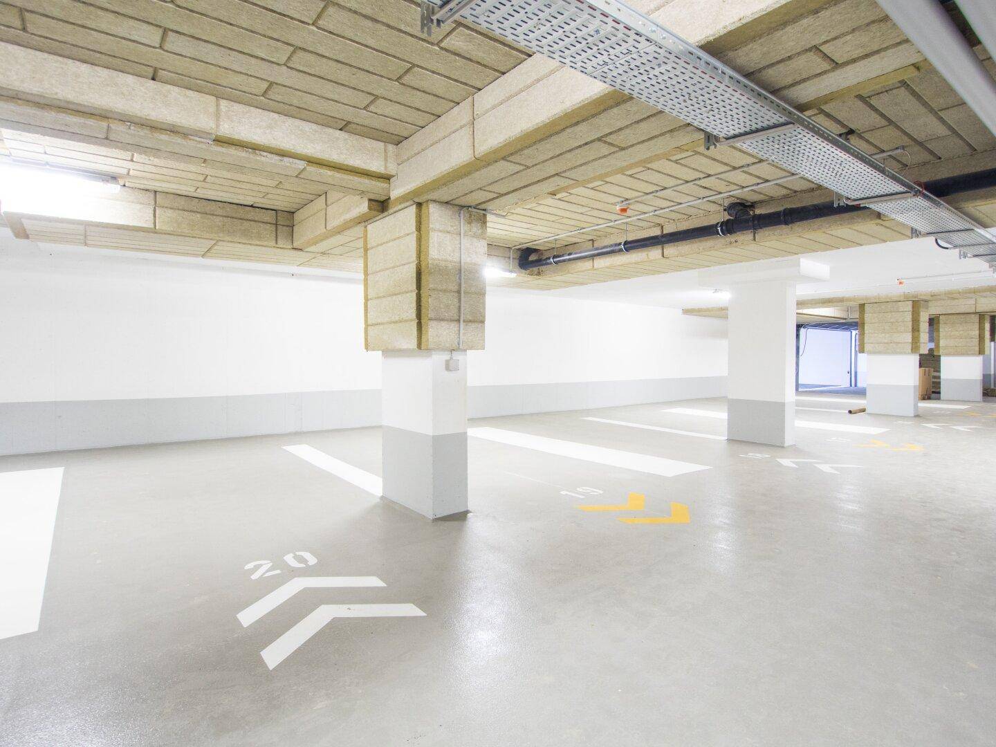 Geräumige Tiefgarage mit markierten Stellplätzen und sichtbaren Installationen an der Decke, die eine funktionale Umgebung bietet.